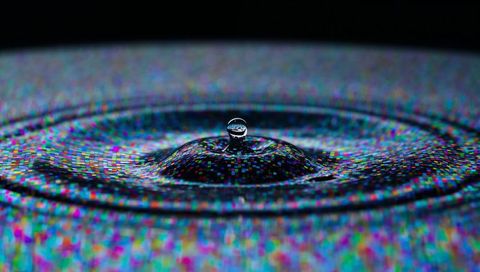 Macro water droplet forming crown while reflecting pixelated led concentric ripples