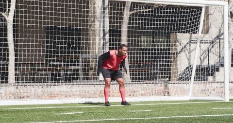 Goalkeeper wearing red concentrating during soccer match guarding goal