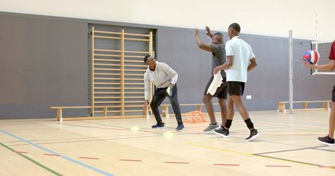 Diverse male teammates practicing volleyball drill on indoor court with cones and net