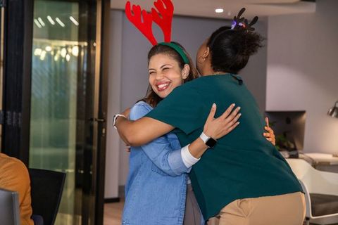 Diverse female coworkers hugging and celebrating with antler headbands in modern office