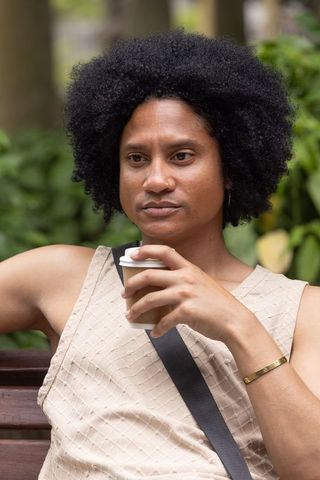 African american man relaxing on park bench holding takeaway coffee cup, casual portrait