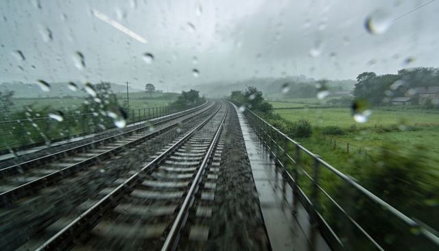 Rain-soaked railway tracks curving through misty countryside with raindrops on window