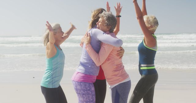 Happy diverse women wearing sports clothes embracing and celebrating at beach. Sport, friendship, healthy and active lifestyle.