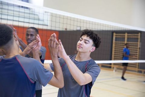 Teen volleyball team celebrating high-five after practice in school gym