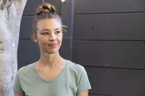 Smiling young woman wearing sage v-neck looking aside on minimalist patio with tree