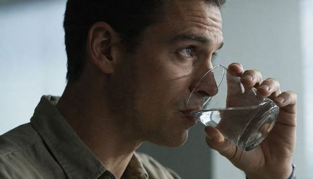 Middle-aged man sipping water from glass near window wearing collared shirt profile