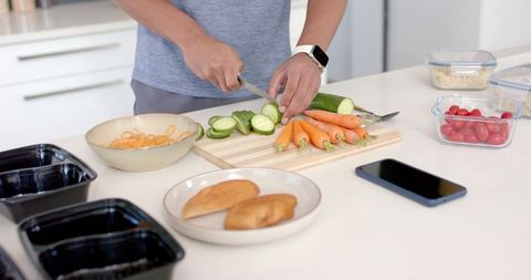 African american man meal-prepping in kitchen slicing cucumber while wearing smartwatch