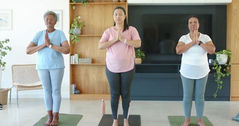 African american women practicing at-home yoga meditation in prayer pose on mats