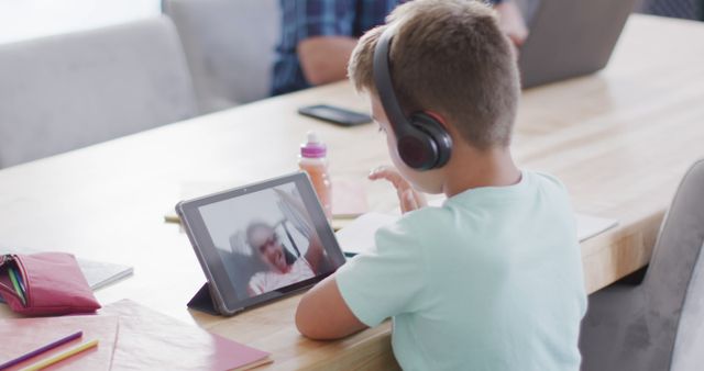This image depicts a young boy wearing headphones chatting on a tablet. Perfect for illustrating concepts of modern technology, online learning, remote communication, and the impact of technology on youth.