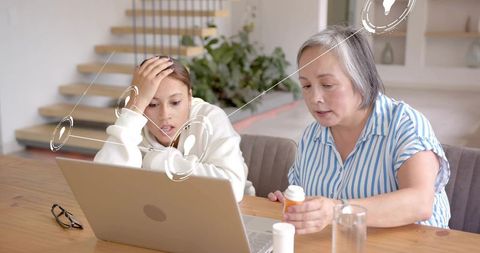Senior caregiver explaining prescription meds with teen using laptop and digital interface