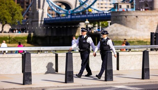 London uniformed police officers patrolling riverfront promenade near tower bridge on sunny day