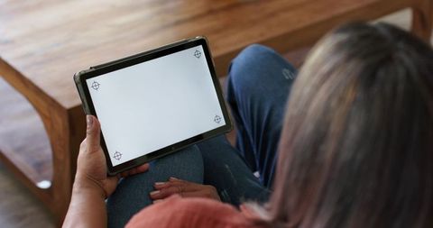 Mature woman holding tablet with blank screen while relaxing in living room