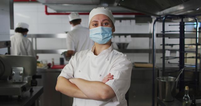 Portrait of caucasian female chef wearing face mask with arms crossed. Health and hygiene in restaurant kitchen during coronavirus covid 19 pandemic.