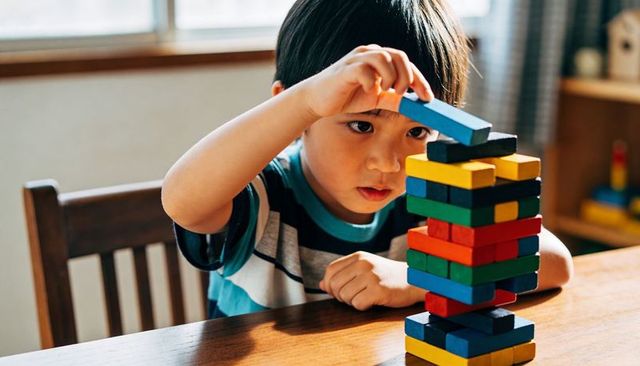 Boy building colorful wooden block tower on table in sunlit room developing fine motor skills