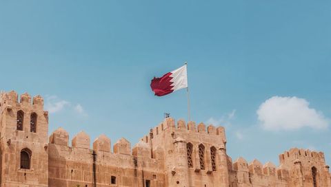 Historic sandstone fortress with maroon-and-white national flag flying against blue sky