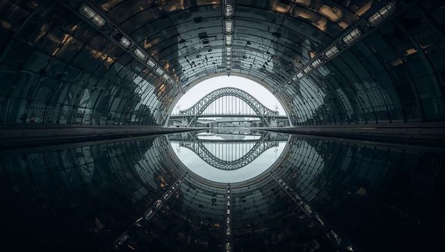 Framing circular tunnel mirroring double-arch steel bridge in perfect water reflection
