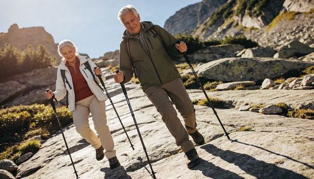 Active senior couple hiking alpine granite ridge with trekking poles and backpacks