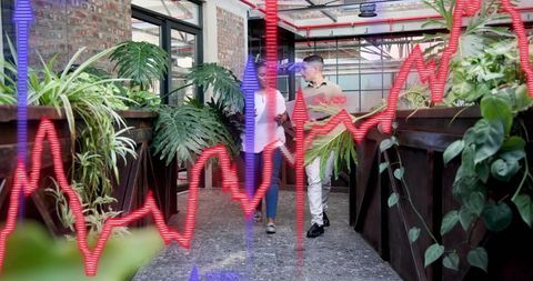 Two colleagues walking and discussing in biophilic office atrium showing financial data