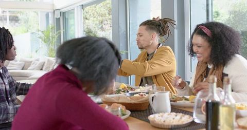 Multicultural friends sharing dinner around sunlit wooden dining table