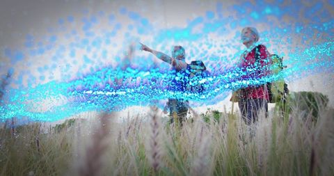 Hikers exploring tall grass meadow with turquoise light trail pointing to horizon