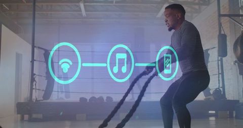 Male athlete powering battle ropes in boxing gym with glowing ar music and mobile icons