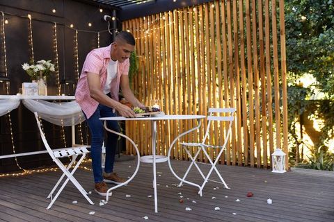 Man arranging fruit platter on decorated backyard deck for romantic outdoor bistro evening