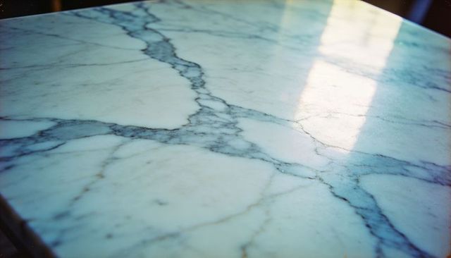 Gleaming round white marble tabletop with bold blue-gray veining and soft window reflection