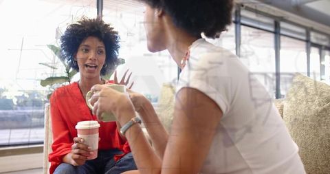 Friends chatting over coffee in modern lounge holding cups casual conversation
