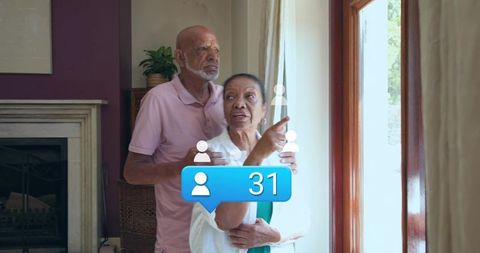 Senior couple gazing through window while pointing and embracing, social notification 31