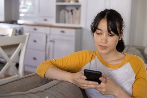 Asian woman relaxing on sofa using smartphone in contemporary interior, casual lifestyle