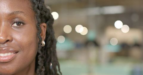 Closeup portrait smiling woman with twisted locs facing camera in open office bokeh lights