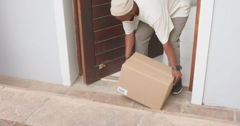 Man placing cardboard delivery box on home doorstep near wooden door with barcode visible