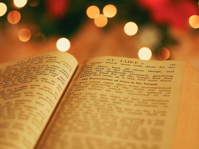 Open Bible showcasing a page of the book of St. Luke, with blurred bokeh lights in the background. Warm and festive ambiance, reflecting themes of faith, spirituality, and holiday traditions. Suitable for religious content, Christmas promotions, church materials, and inspirational messages.