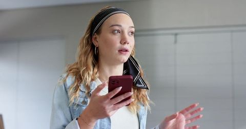 Young woman holding smartphone and speaking while gesturing in bright minimalist interior