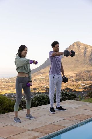 Diverse Friends Exercising with Dumbbells by Scenic Open Poolside
