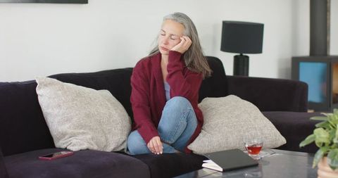 Mature woman resting on sofa in burgundy cardigan, contemplative cozy moment at home
