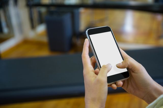 Woman holding and using a mobile phone in a gym. Ideal for illustrating concepts related to fitness, technology, communication, and multitasking. Useful for fitness apps, gym advertisements, and articles on staying connected while working out.
