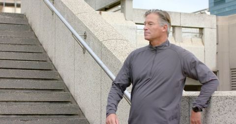 Middle-aged man leaning on concrete railing near urban staircase, looking thoughtful