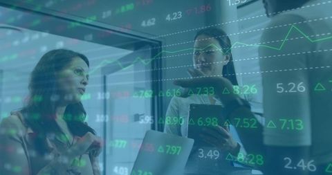 Business Women Discussing Market Charts Overlaid with Financial Data on Laptop and Tablet