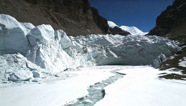 Sunlit crevassed glacier icefall in alpine valley with sinuous meltwater channel, seracs