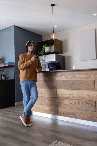 African american man leaning at wooden cafe counter holding smartphone and looking left