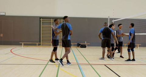 Diverse male volleyball team practicing together and shaking hands in school gym court