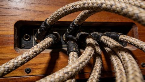 Cloth-braided audio cables plugging into recessed metal panel on varnished wood console