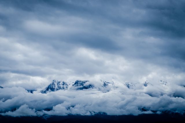 Snow-capped mountains are partially obscured by a dramatic, cloudy sky, creating an atmosphere of mystery and calm in this natural wilderness landscape. Suitable for travel websites, nature blogs, inspirational posters, background elements in presentations emphasizing strength and serenity.