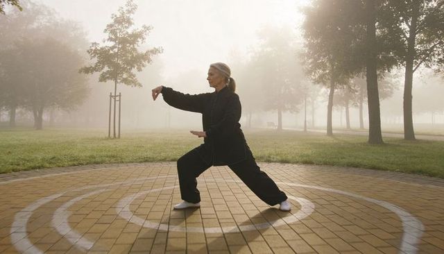 Senior woman practicing tai chi on concentric rings in misty park at dawn for wellness
