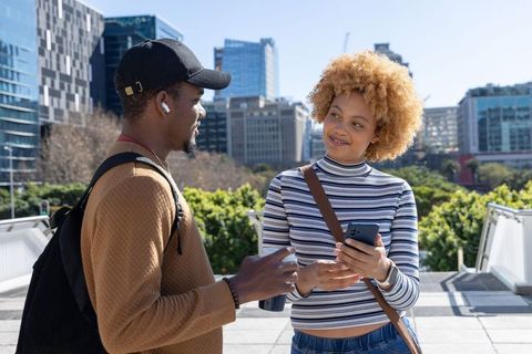 Young diverse friends chatting and smiling on urban terrace holding smartphone and coffee