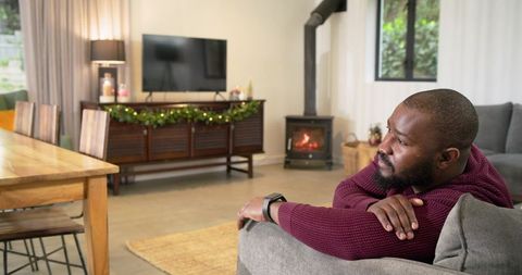 African american man relaxing on sofa in cozy living room with fireplace and holiday garland