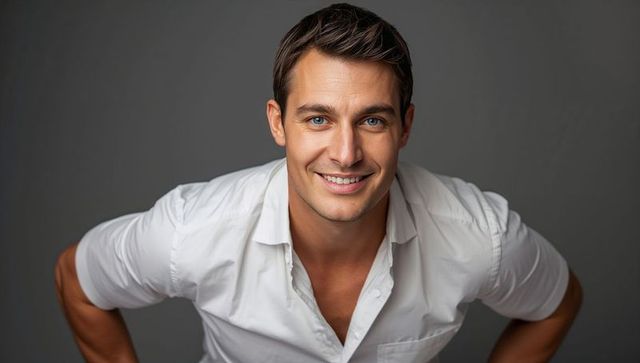Confident smiling man leaning forward in white shirt, closeup headshot on gray background