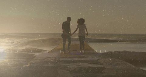 Couple walking hand in hand on pier at sunset holding guitar with grainy film glow