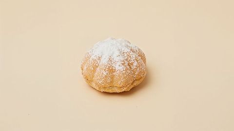 Pumpkin-Shaped Gourmet Pastry with Powdered Sugar on Beige Surface